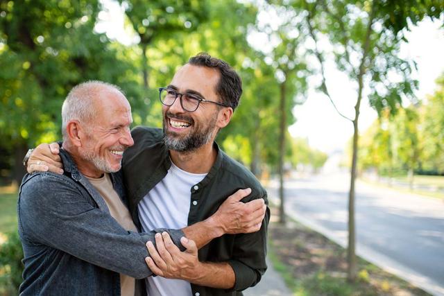 Uomo anziano e un giovane si abbracciano lungo un viale alberato