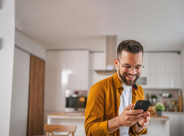 Ragazzo guarda il telefono soddisfatto nella cucina di casa